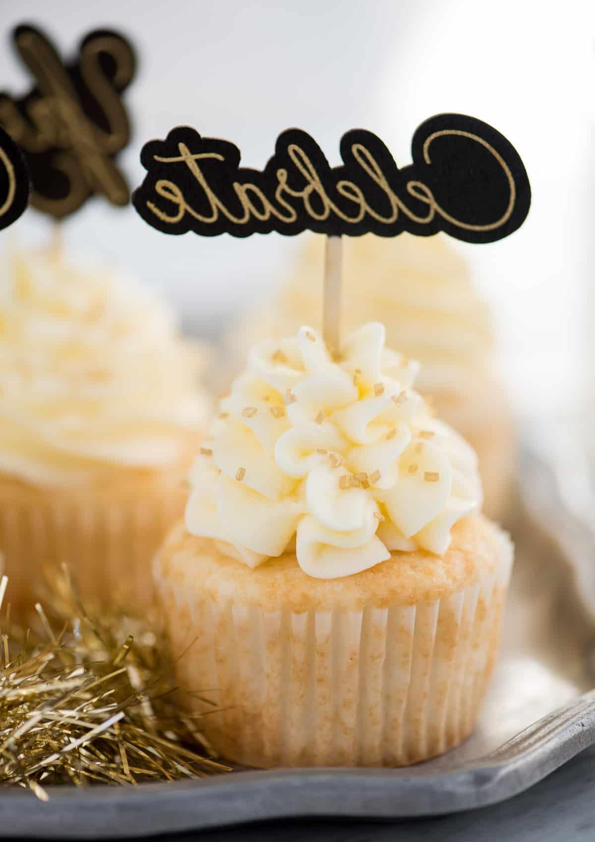 Questa ricetta facile per cupcakes allo champagne con glassa allo champagne è un dessert di Capodanno da non perdere! Come fare i cupcakes allo champagne usando una torta in scatola. Facili cupcakes allo champagne con glassa al burro e champagne, decorati con zuccherini dorati e un topper per cupcake con la scritta "celebrate"