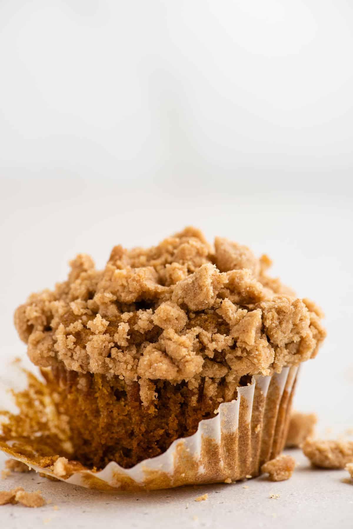 Muffin alla Zucca e Streusel Senza Glutine 5 Un singolo muffin di zucca senza glutine con il rivestimento parzialmente rimosso su sfondo bianco