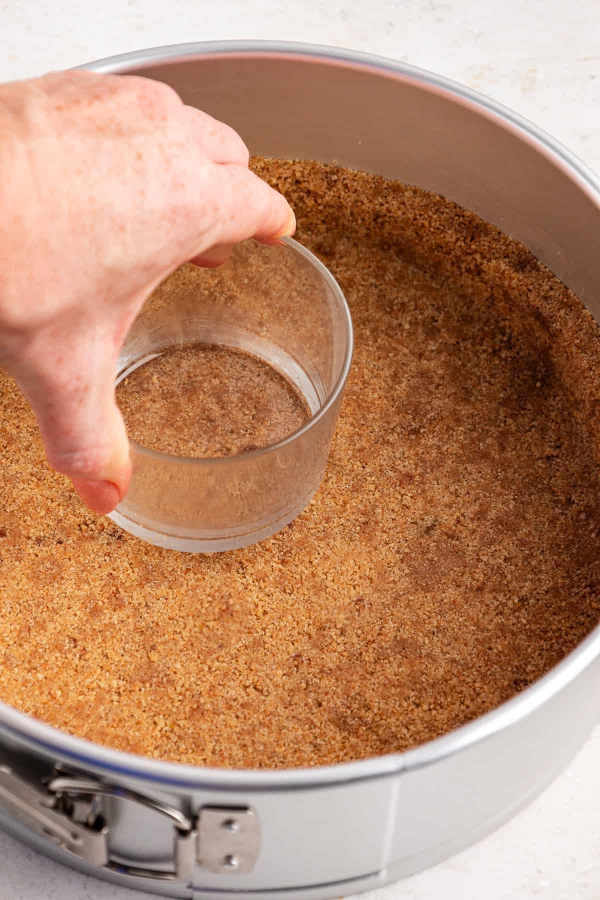 La Migliore Ricetta per Cheesecake alla Torta Pecan 6 Base di biscotti graham pressata in una tortiera a cerniera con un bicchiere
