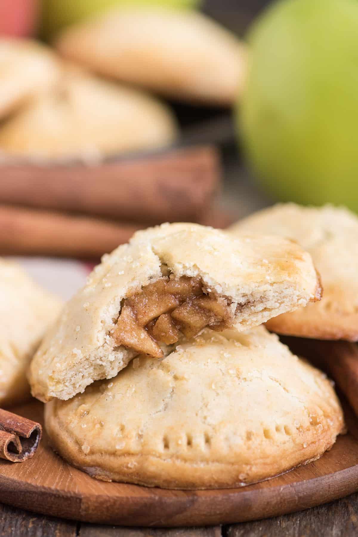 Le tortine di mele fatte in casa sono un ottimo dessert alle mele da preparare in qualsiasi momento dell'anno. Guarda il video rapido passo dopo passo per imparare a fare queste mini torte di mele. #tortinedimele #minitorte #tortadimele #dolcettiallemele Tortine di mele su uno sfondo di legno con una mela verde sullo sfondo