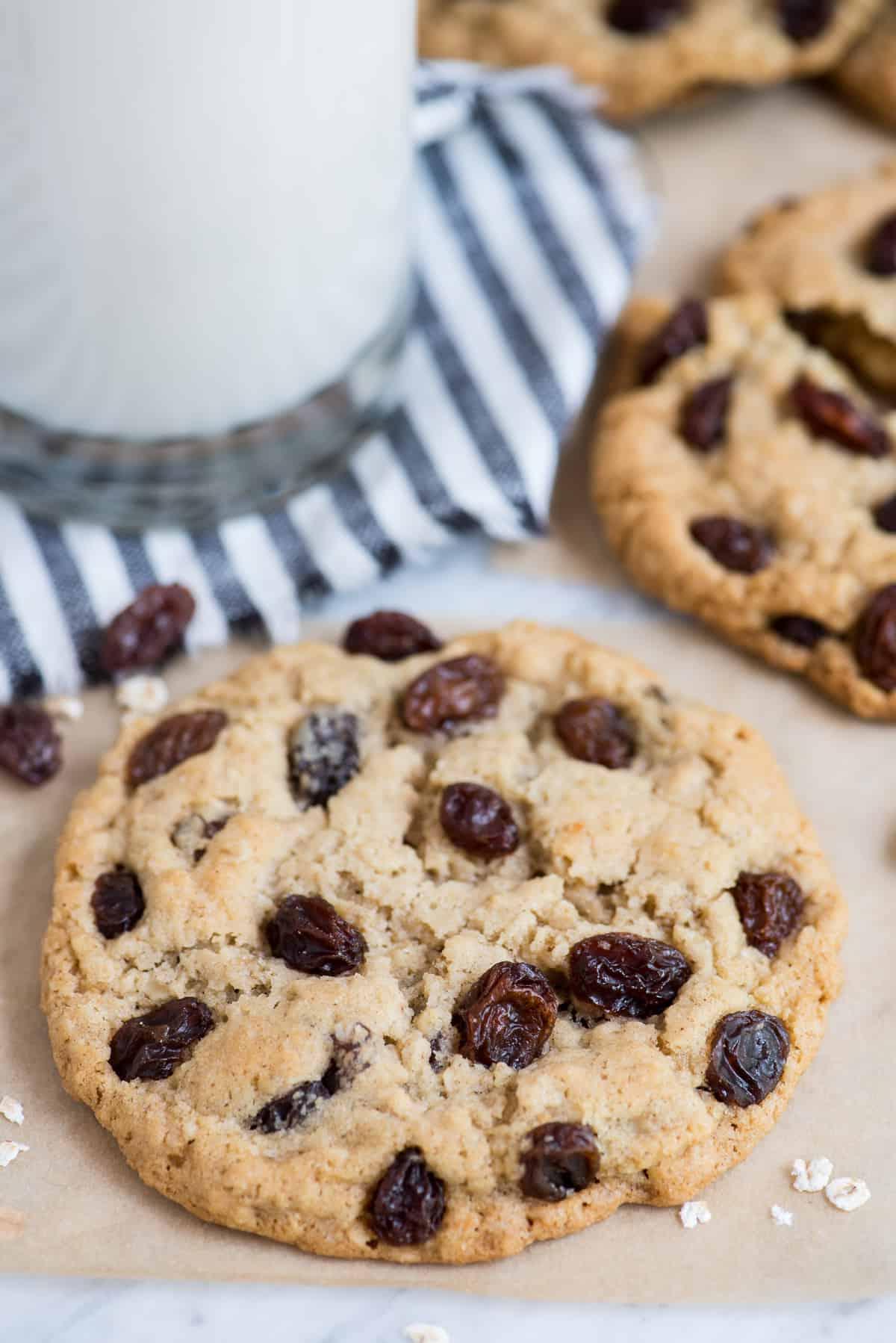 Biscotti all'avena e uvetta fatti in casa 7 Biscotto avena e uvetta su carta forno marrone con un biscotto e un bicchiere di latte sullo sfondo
