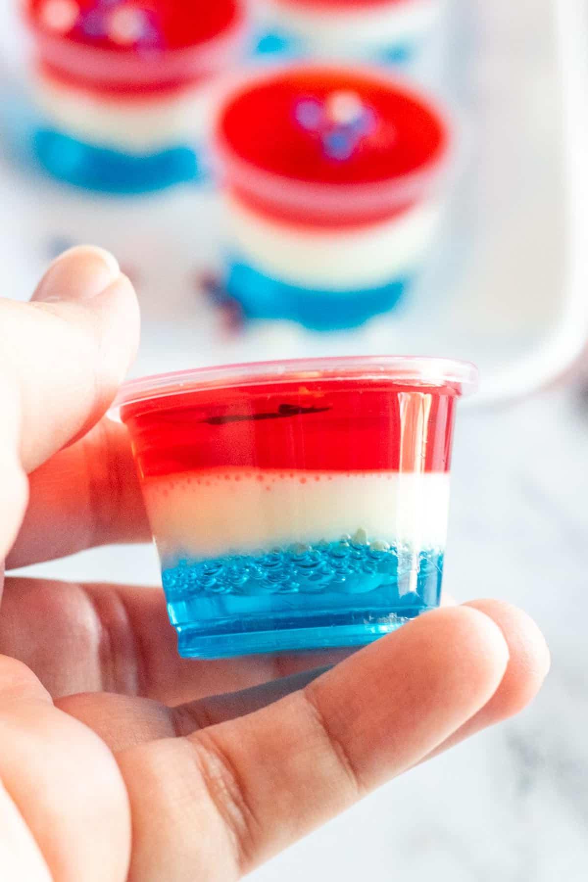 Shot di Gelatina Rossi, Bianchi e Blu con Vodka 7 Mano che tiene uno shot di gelatina patriottico