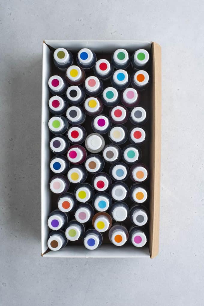 Glassa Reale senza Polvere di Meringa 7 vista dall'alto di una scatola piena di flaconi di coloranti alimentari in gel con puntini colorati in cima che mostrano il colore di ciascuno