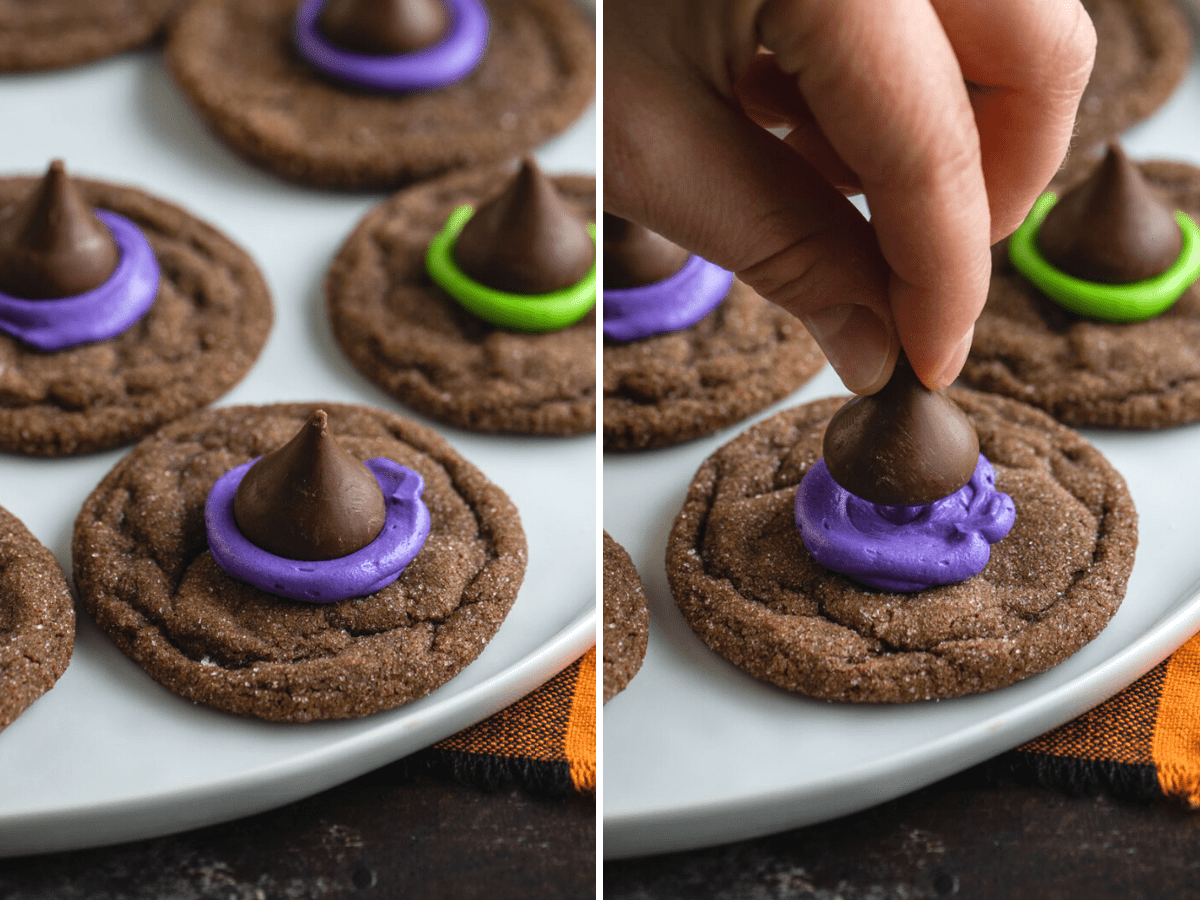 Morbidi biscotti al cioccolato sormontati da un bacio di cioccolato, glassa e zuccherini, questi Biscotti Cappello da Strega sono un dessert di Halloween facile. Una mano che posiziona un bacio di Hershey's sulla glassa su un biscotto