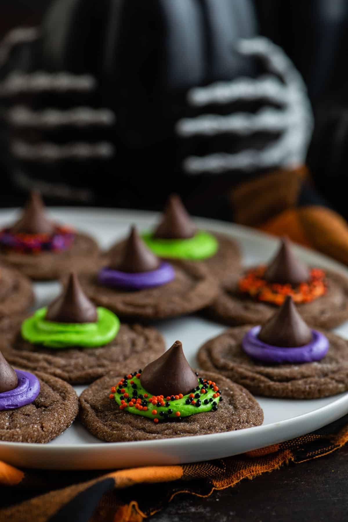 Morbidi biscotti al cioccolato sormontati da un bacio di cioccolato, glassa e zuccherini, questi Biscotti Cappello da Strega sono un dessert di Halloween facile. Un piatto di biscotti a forma di cappello da strega