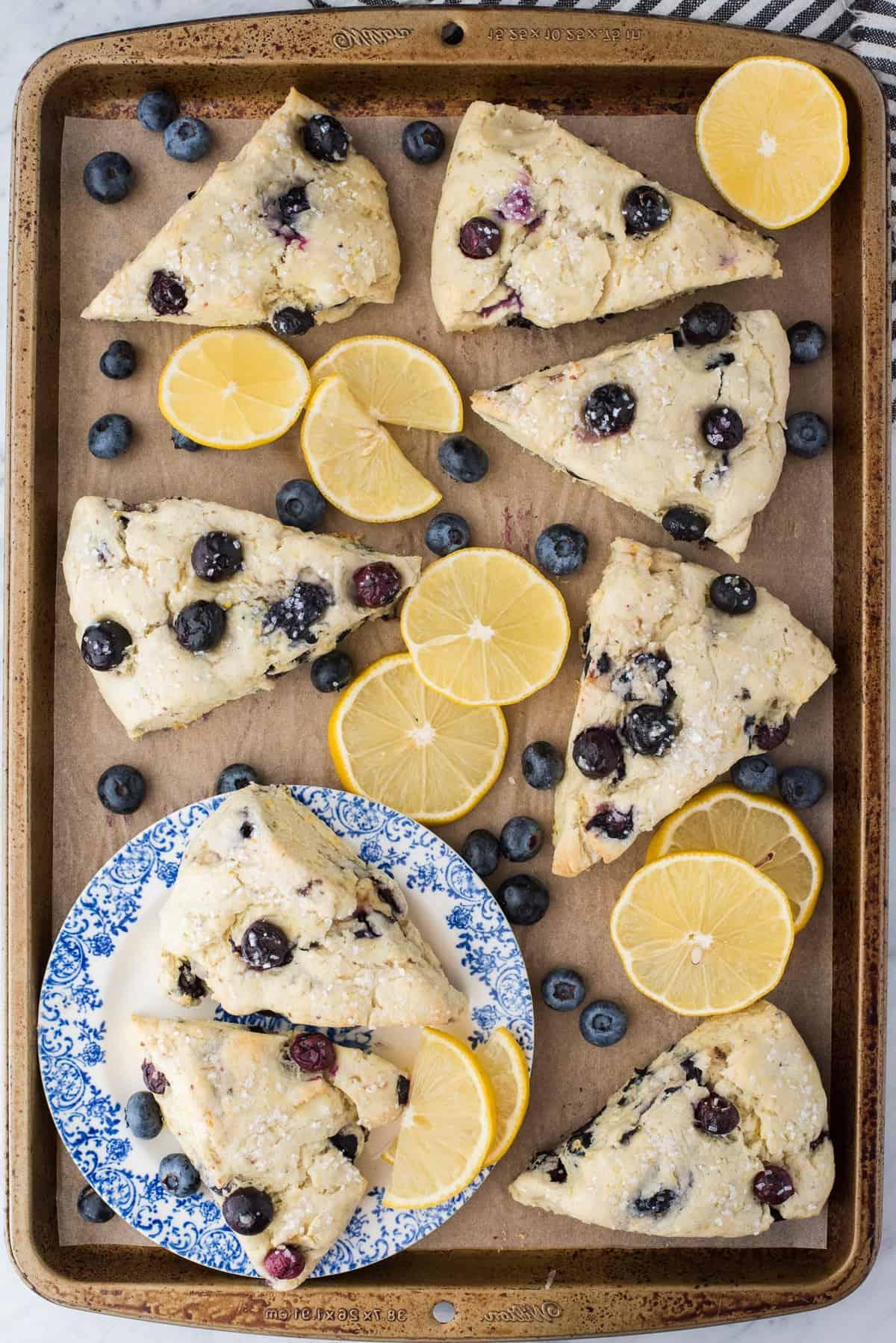 I Migliori Scones al Limone e Mirtilli 9 Scones al limone e mirtilli su carta forno marrone con fette di limone e mirtilli