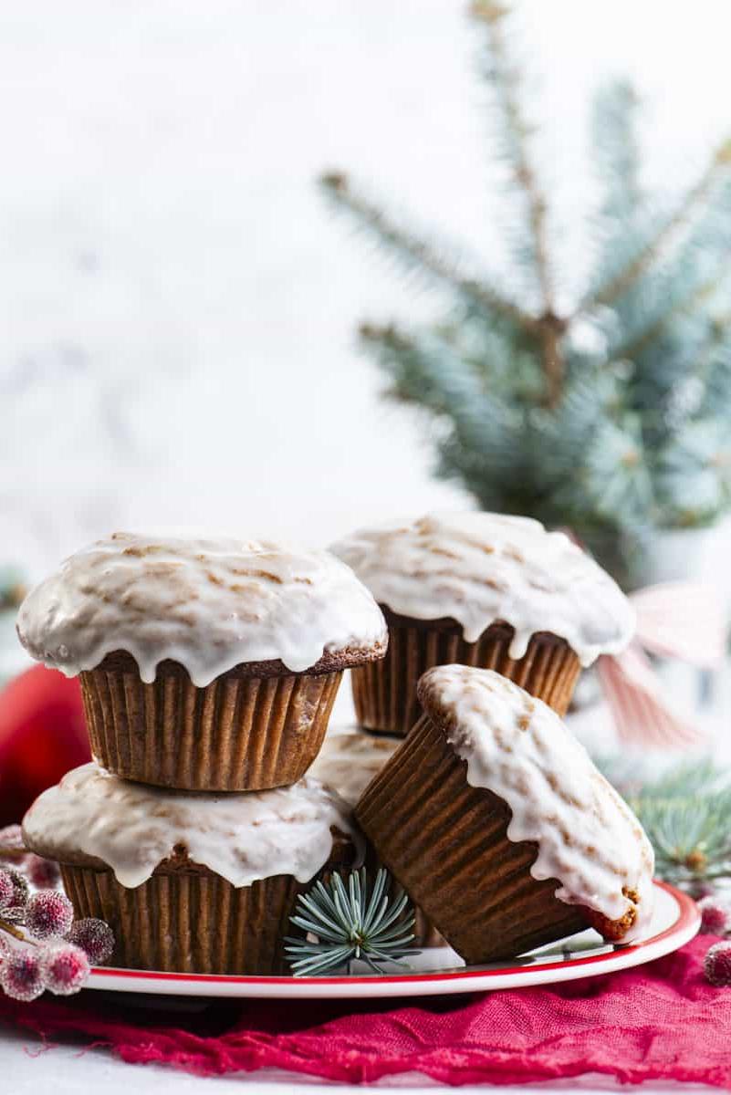 Muffin al pan di zenzero 9 Muffin al pan di zenzero con glassa alla vaniglia disposti su un piatto bianco con bacche rosse zuccherate e rami di abete sempreverdi