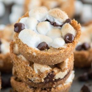 Coppette S'mores 2 Tre Tazze S'mores da Forno impilate, circondate da altre deliziose s'mores cups su un piatto da forno.