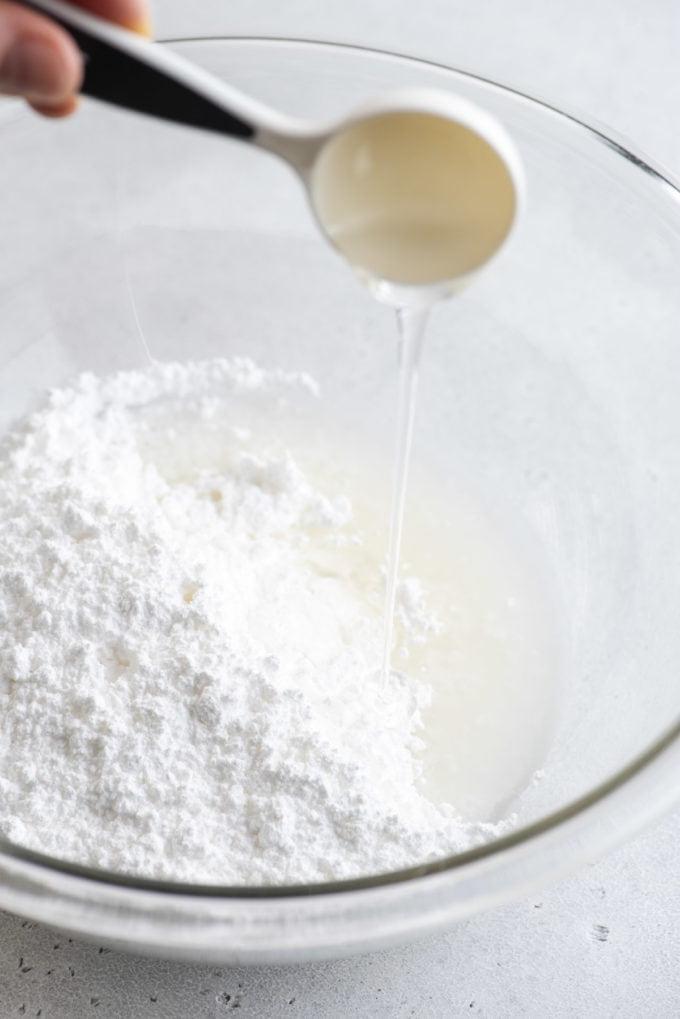 Glassa Reale senza Polvere di Meringa 9 sciroppo di mais aggiunto a una ciotola di vetro trasparente con ingredienti per ghiaccia reale