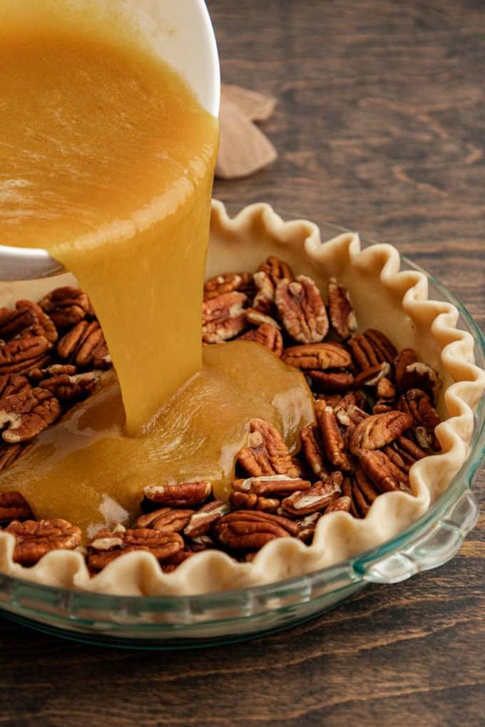 Torta di Noci Pecan Casereccia All'Antica 9 Una teglia di vetro poggiata su una superficie di legno con noci pecan all'interno, e il composto del ripieno della torta di noci pecan viene versato sopra