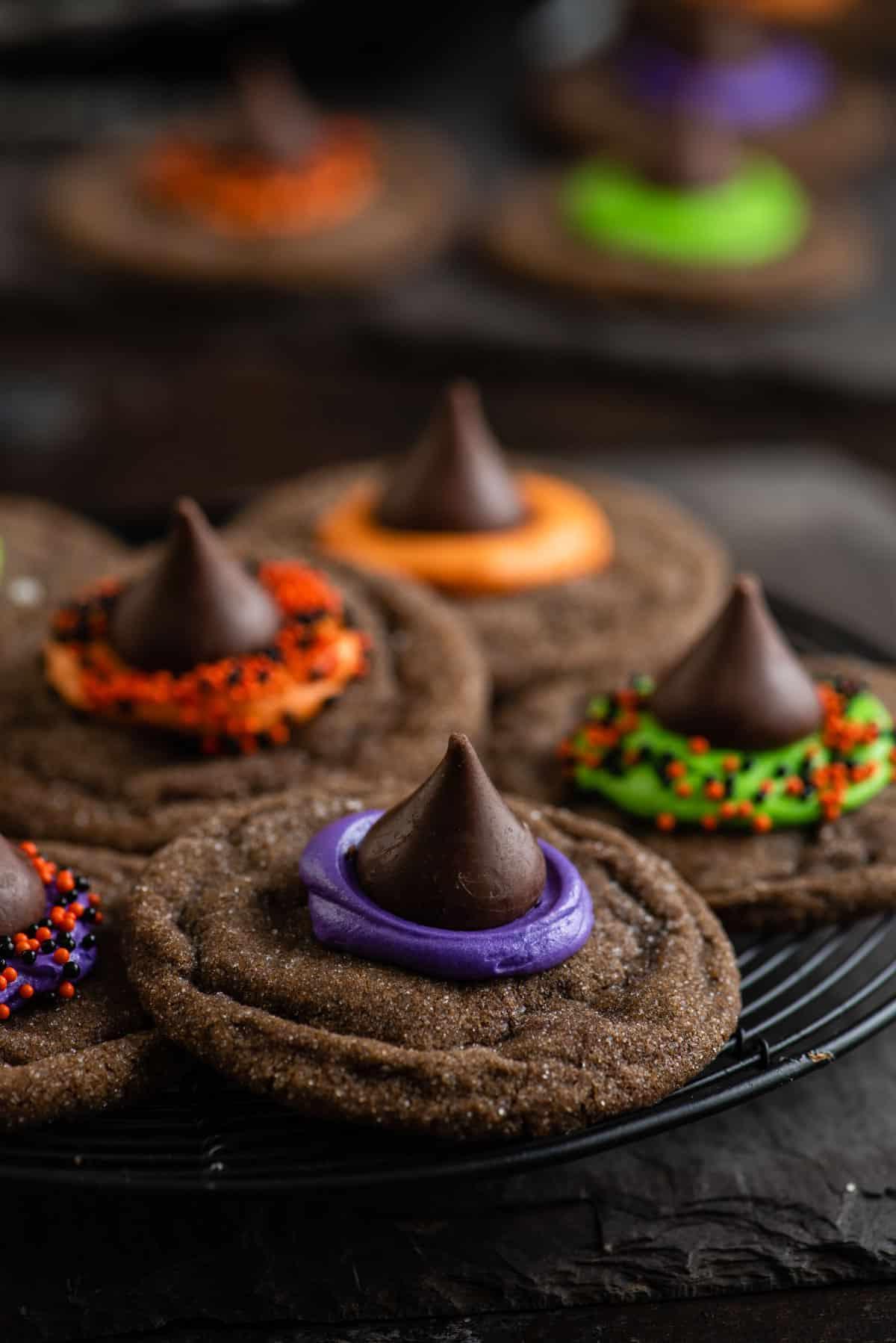 Morbidi biscotti al cioccolato sormontati da un bacio di cioccolato, glassa e zuccherini, questi Biscotti Cappello da Strega sono un dessert di Halloween facile. Primo piano di biscotti a forma di cappello da strega