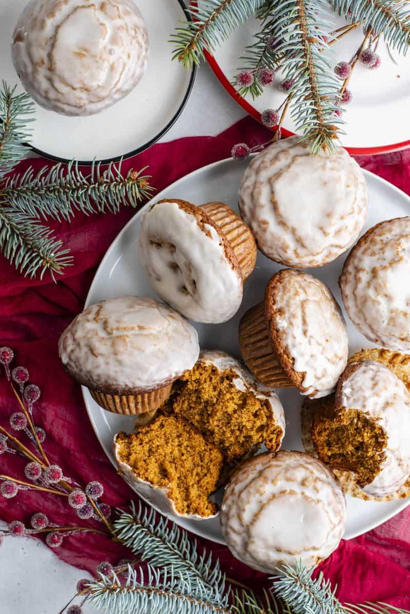 Muffin al pan di zenzero 10 Muffin al pan di zenzero con glassa alla vaniglia disposti su un piatto bianco con bacche rosse zuccherate e rami di abete sempreverdi
