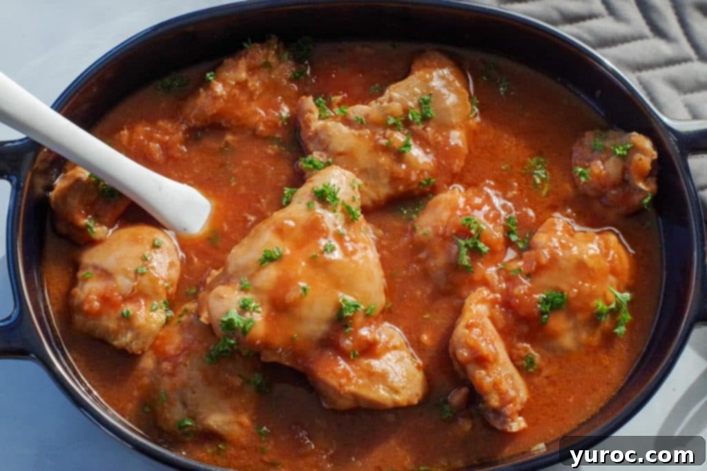 chicken in a hurry in a dark blue oval casserole dish, with a marble spatula, on a marble counter surface, with a grey oven mitt in the background
