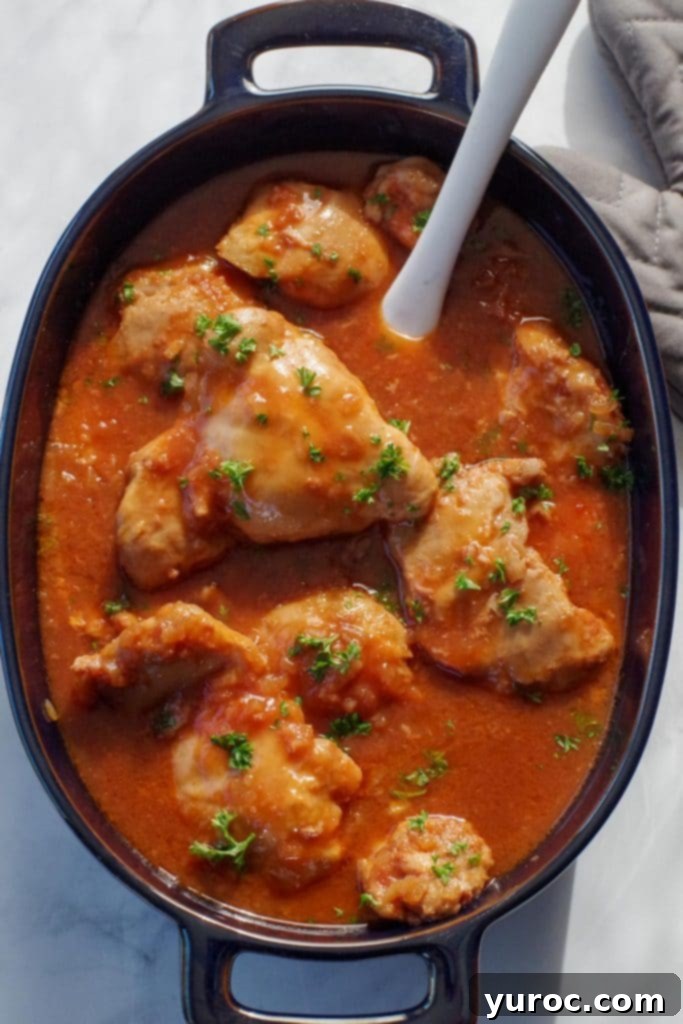 chicken in a hurry in a dark blue oval casserole dish, with a marble spatula, on a marble counter surface, with a grey oven mitt in the background