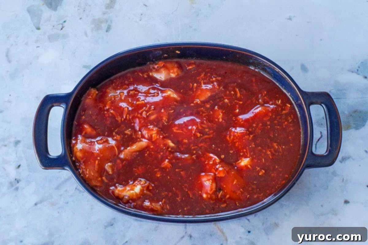 Sauce poured over raw chicken thighs in blue casserole dish.