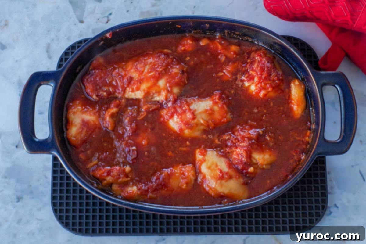 Cooked chicken in sauce in blue casserole dish.