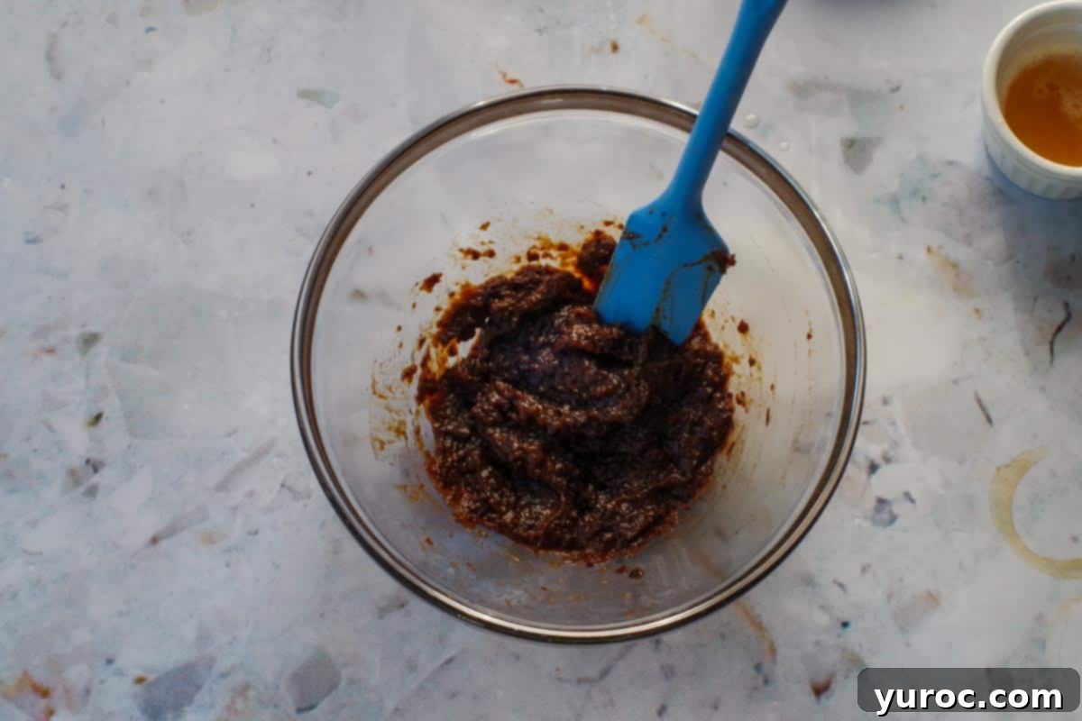 Prunes pureed with water in medium glass bowl with blue spatula.