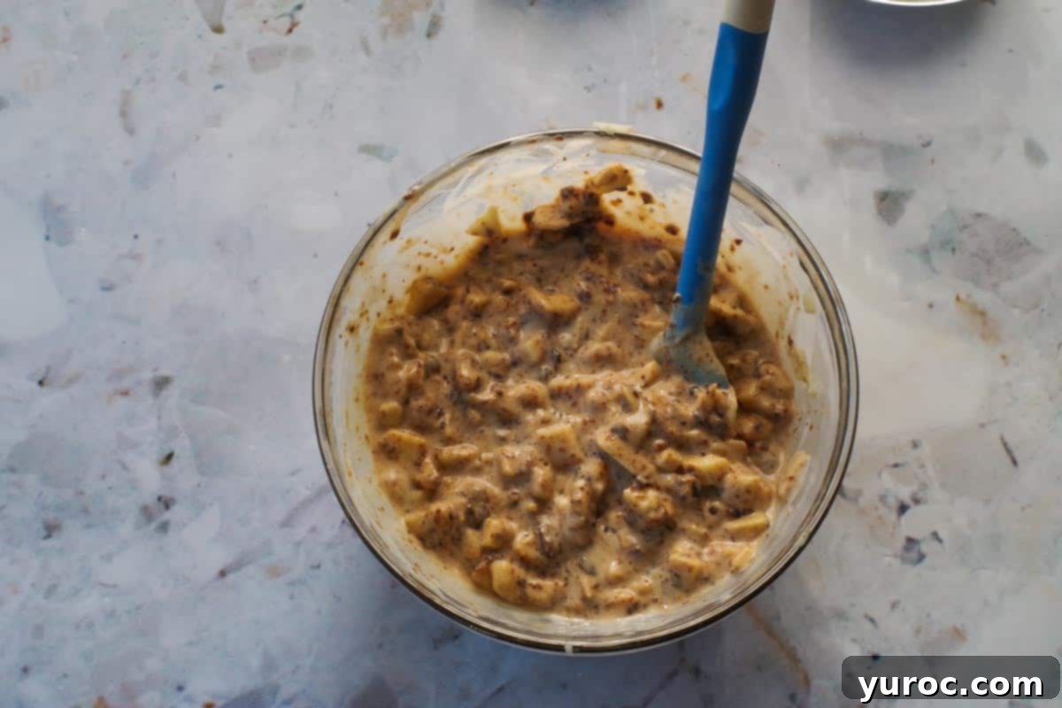 Prunes and coconut milk added to apple mixture in medium glass bowl with blue spatula.