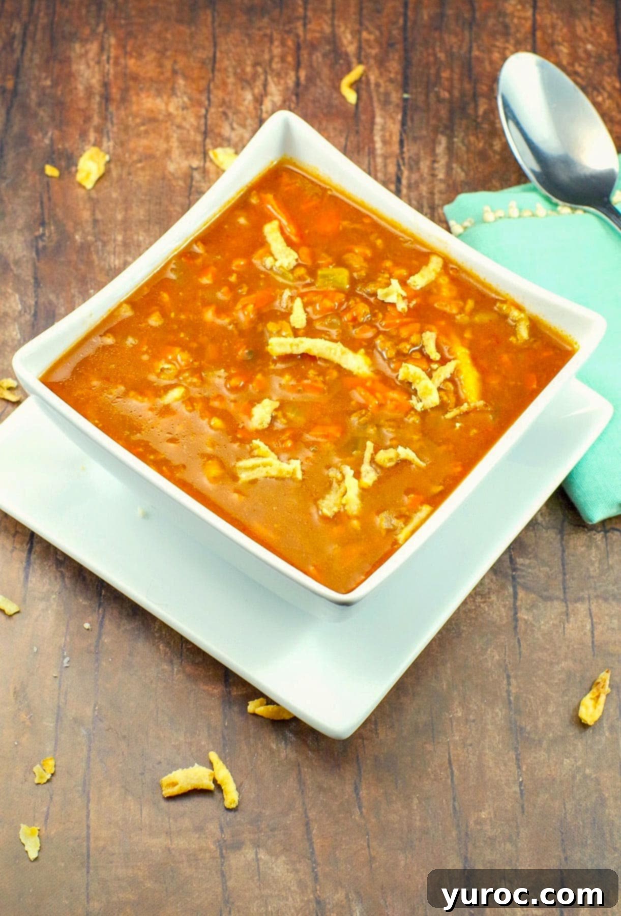 Award-winning Shredded Carrot Chowder 9 healthy carrot soup in a white bowl, on a white plate, on brown faux wooden surface, with pastel green napkin on right side and crispy onions on soup and scattered on surface