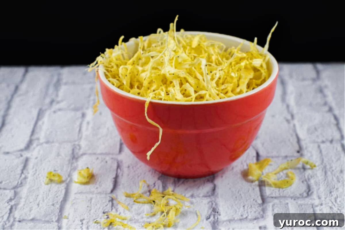 Deep-fried parsnip crisps in an vibrant orange bowl on a clean white surface, showcasing their golden crunch.