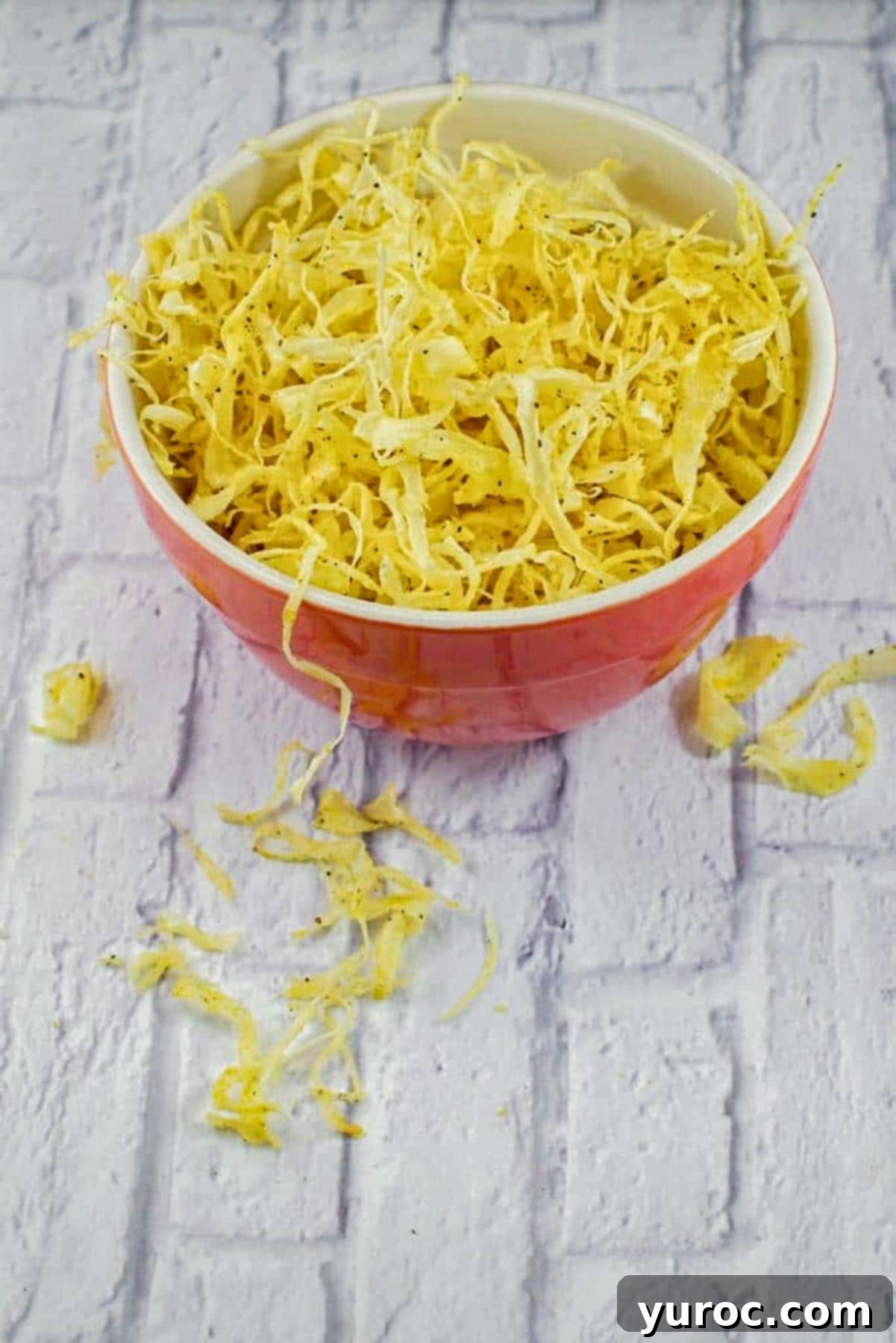 A bountiful pile of golden fried parsnip crisps in a bright orange bowl, positioned on a clean white countertop.