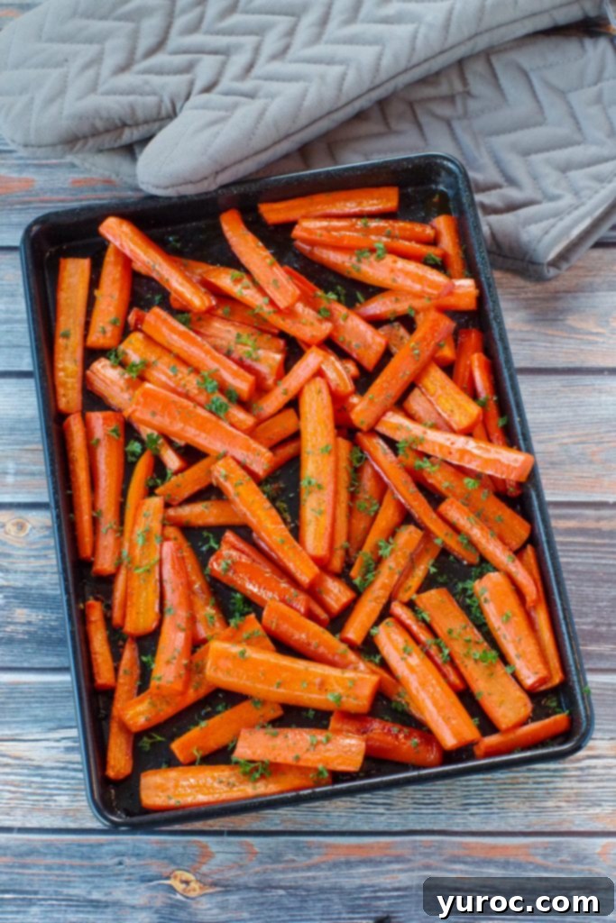Wholesome Brown Sugar Glazed Carrots 7 Roasted carrots with brown sugar on a black sheet pan on a blue faux wood surface, showcasing the beautiful caramelization.