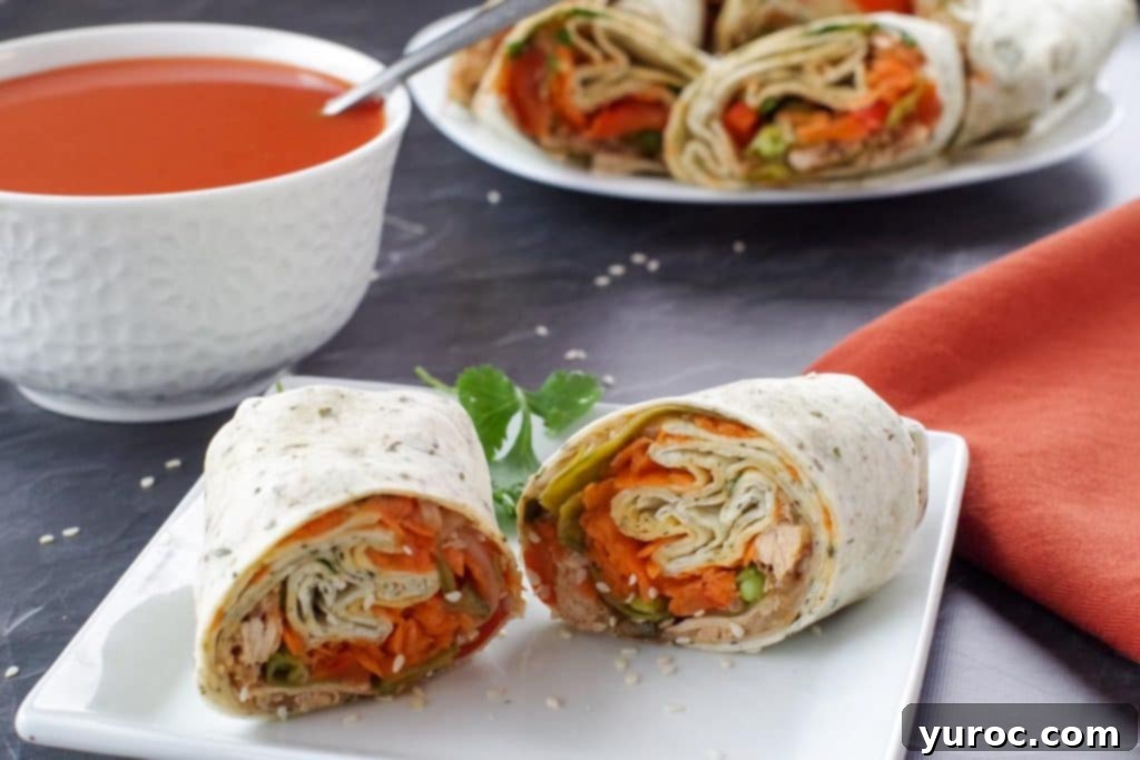 healthy turkey wrap, sliced in half, on white plate, with bowl of tomato soup and platter of turkey wraps in the background