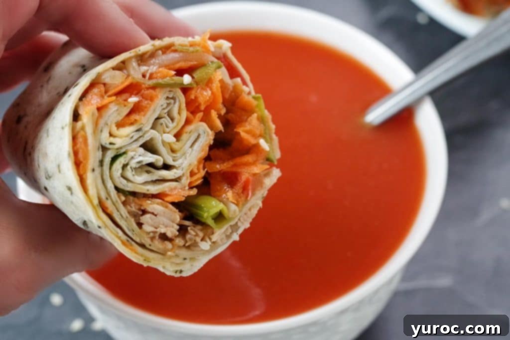 half a turkey wrap being held up over a bowl of tomato soup