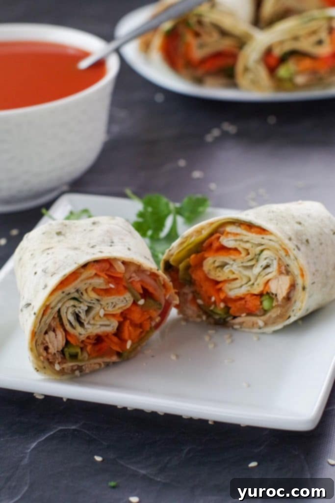 healthy leftover turkey wrap, sliced in half, on white plate, with bowl of tomato soup and platter of turkey wraps in the background
