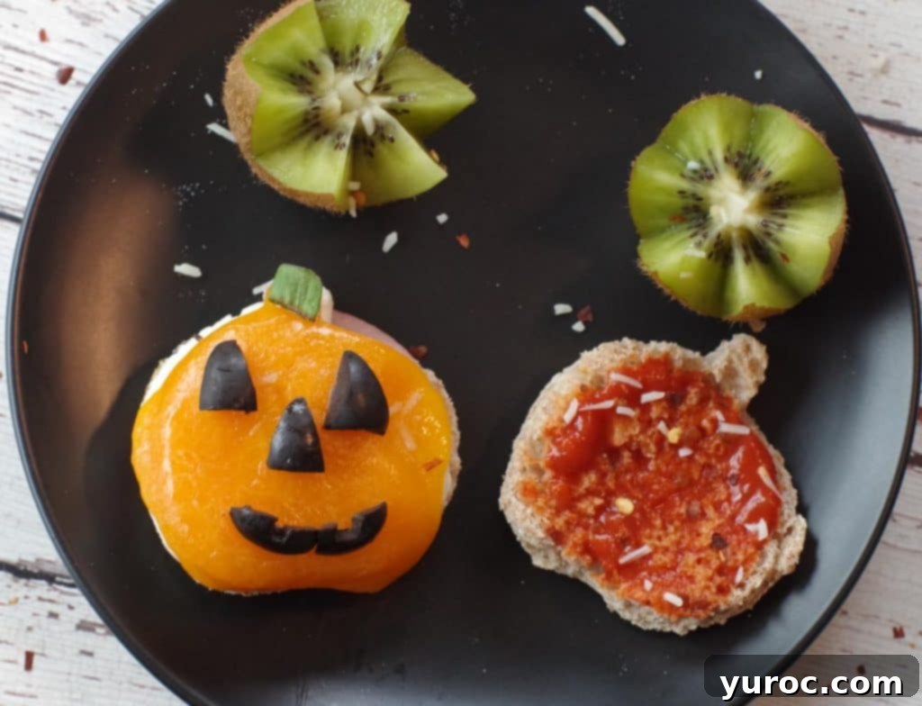 Halloween Breakfast Pizza Sandwich cut into a jack o'lantern on a black plate with kiwi flowers