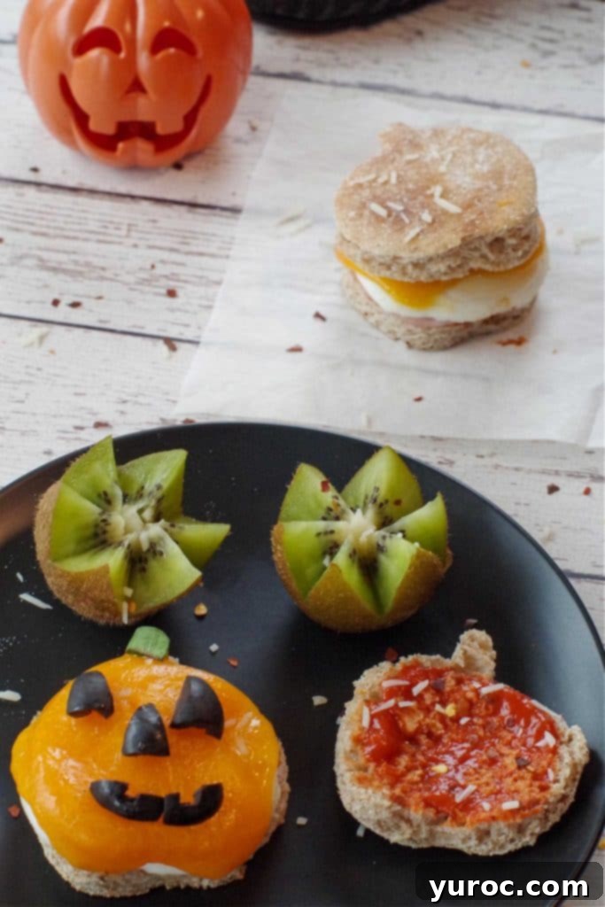 Halloween Breakfast Pizza Sandwich cut into a jack o'lantern on a black plate with kiwi flowers with whole sandwich and plastic jack o'lantern in the background