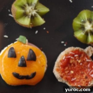 Halloween Breakfast Pizza Sandwich cut into a jack o'lantern on a black plate with kiwi flowers