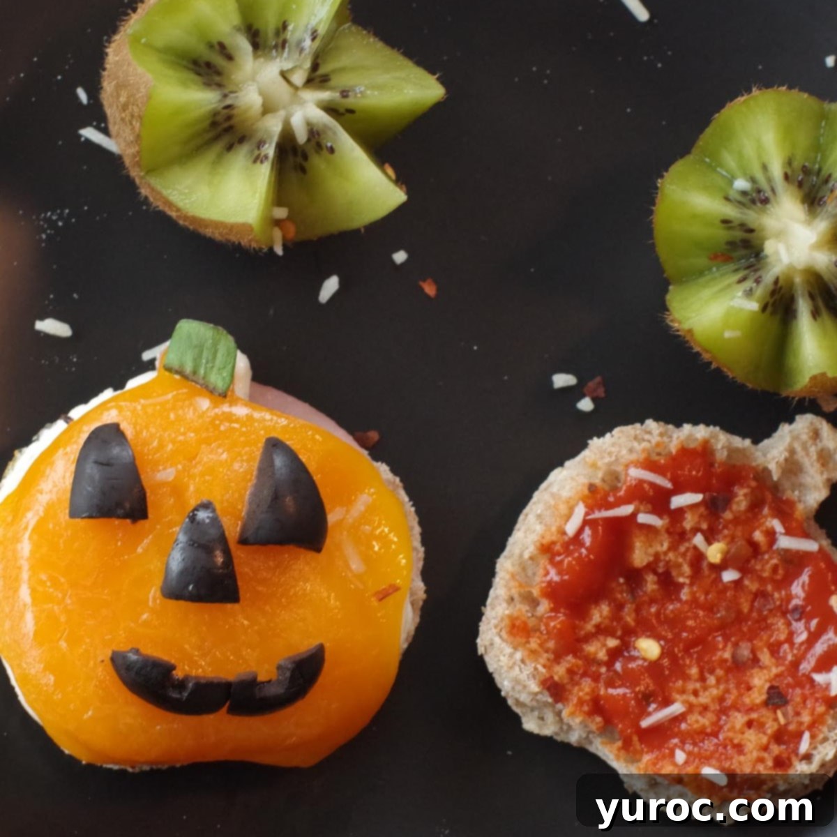 Halloween Breakfast Pizza Sandwich cut into a jack o'lantern on a black plate with kiwi flowers