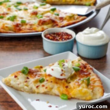 piece of perogy pizza on a white plate with whole pizza and small bowl of chili flakes and sour cream in the background
