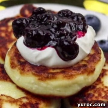 syrniki pancakes stacked with sour cream and blueberry sauce