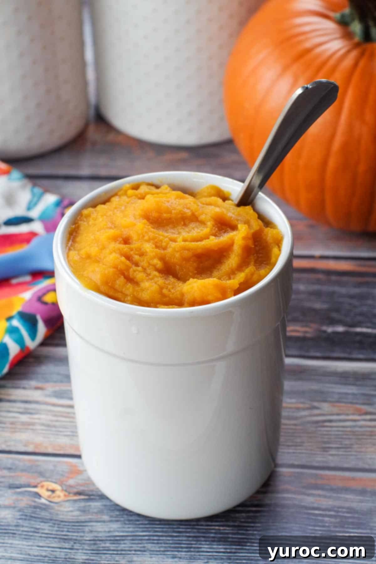 Unlock the Secrets of Whole Pumpkin Cooking and Homemade Purée 18 white canister with pumpkin puree in it, as well as spoon and whole pumpkin in background