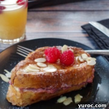 French Toast Sandwich on a black plate with fork and glass of juice in background