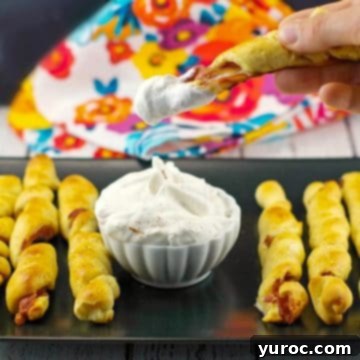 breakfast pigs in a blanket on black tray with dip in the middle and one being dipped into dip
