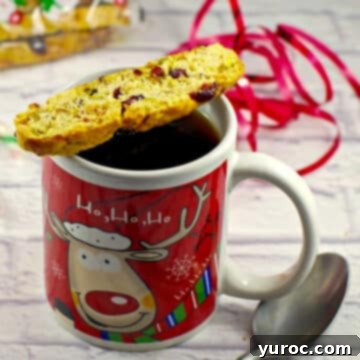 Christmas biscotti sitting on a Christmas mug of coffee with a spoon to the right
