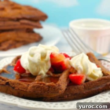 chocolate waffles with strawberries and whipped cream on a white plate white with a stack of waffles in background