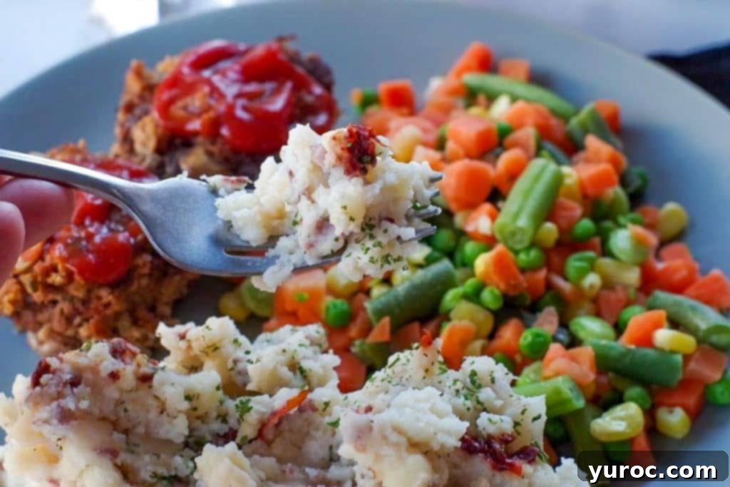 Chipotle mashed potatoes being held up on a fork over a plate with mashed potatoes, mini meat loaves and mixed vegetables.