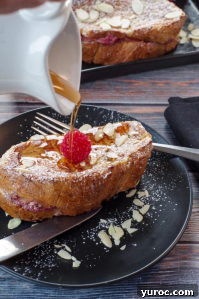Raspberry Cream-Filled French Toast Sandwich 7 French Toast Sandwich on a black plate with fork and syrup being poured onto it