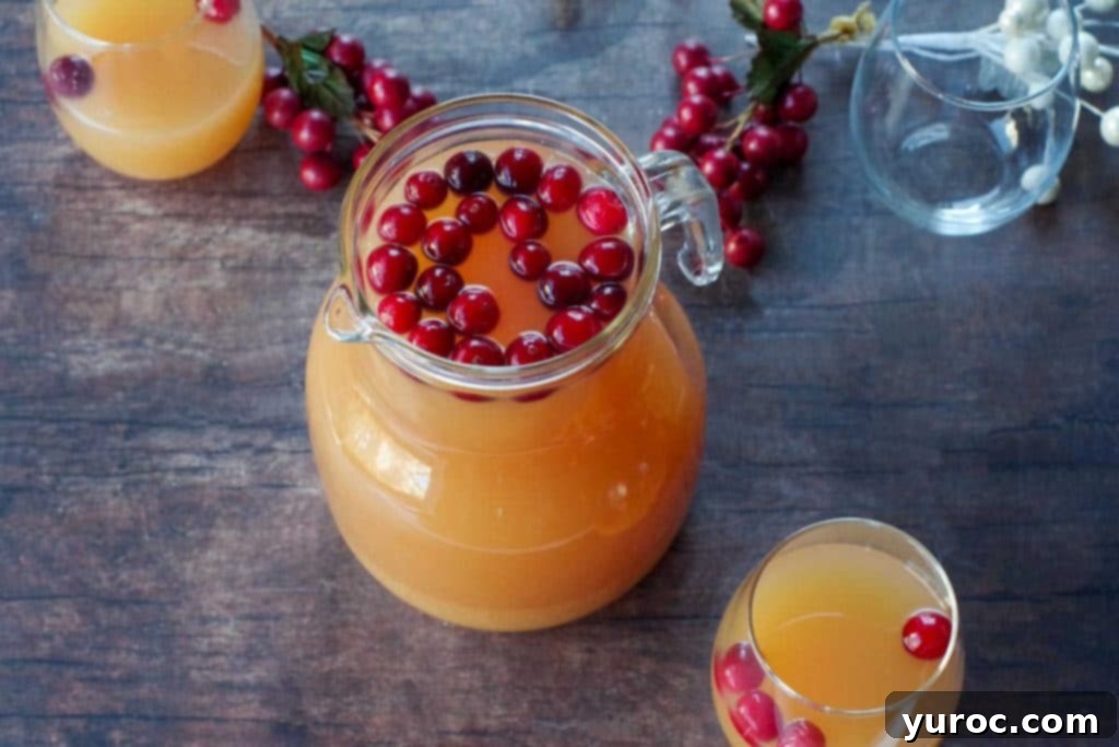 Merry Berry Brunch Sparkler 4 Cranberry orange punch in a clear glass pitcher with individual glasses and fresh cranberries in the background.