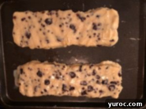 Close-up of biscotti dough logs being brushed with egg wash before baking.