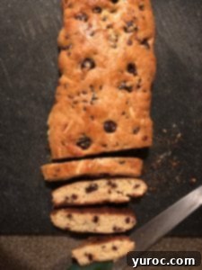 Hands demonstrating how to slice a baked biscotti log diagonally into individual cookies.