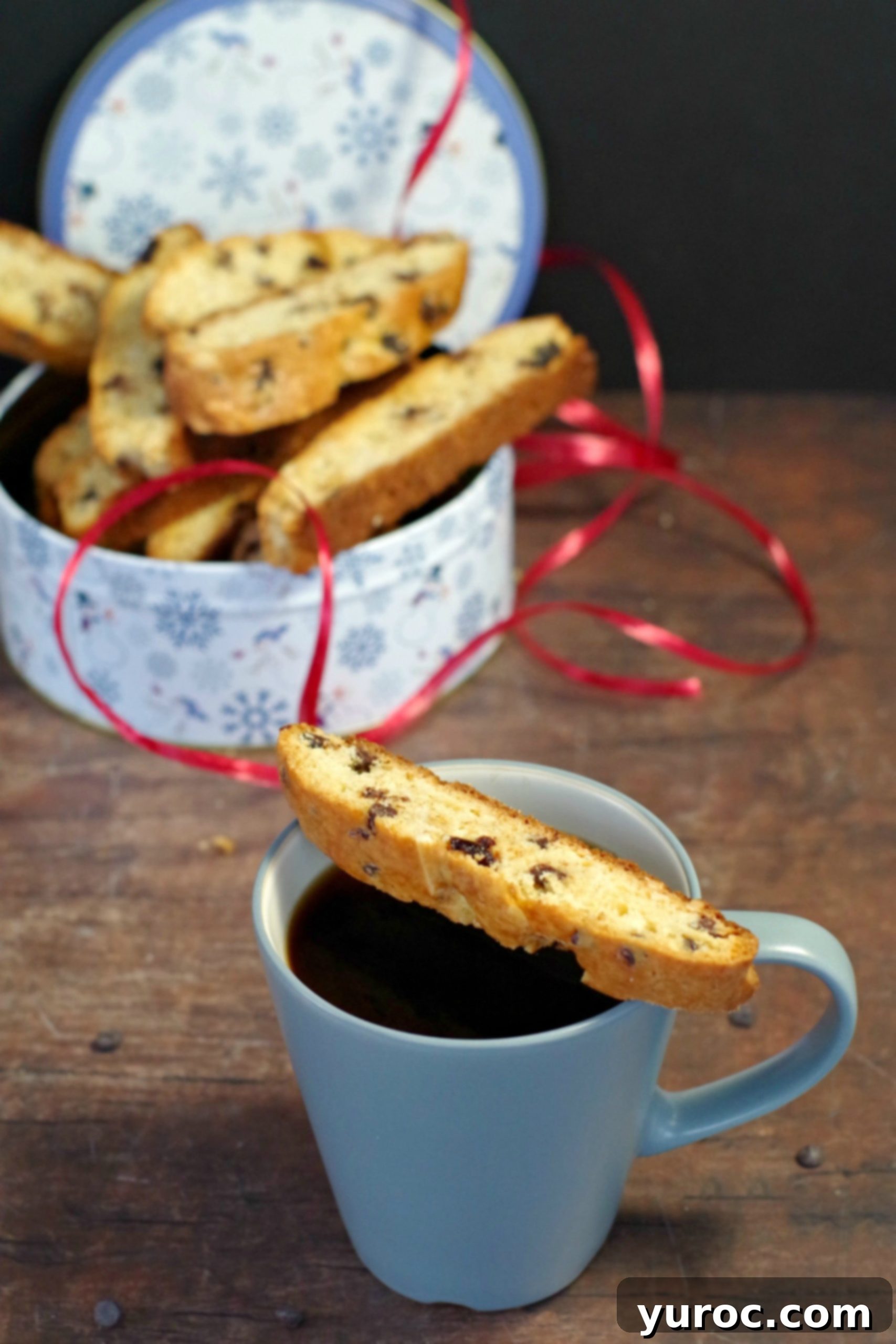 Beautifully arranged Black Forest biscotti on a blue mug, with a charming Christmas tin filled with more biscotti in the background, ready for gifting or enjoying.