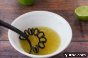 whisk mixing lime juice, honey and lime zest in white bowl