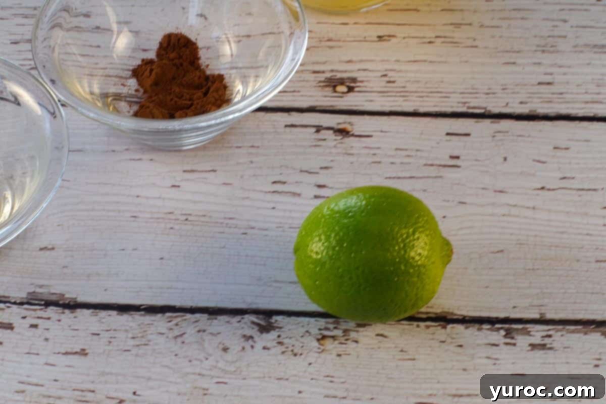 A lime on a faux wooden surface with a small glass bowl of cinnamon in the background.