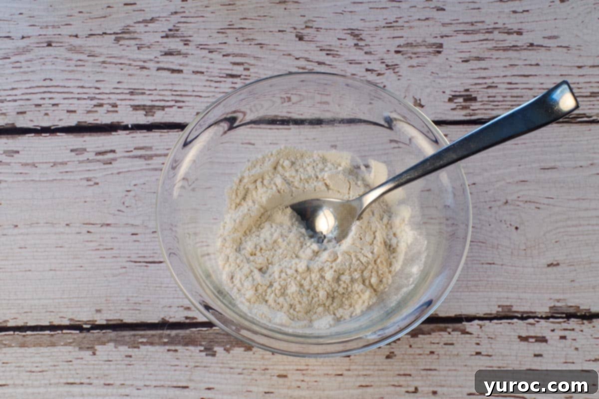 Flour and baking powder mixed together in a small glass bowl with a tablespoon in the bowl.