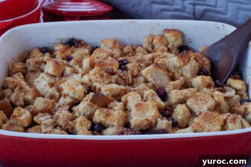 Festive Cranberry Bread Pudding 6 bread pudding with condensed milk in a red casserole dish the a wooden spoon in it and red dishes and grey oven mitts in background